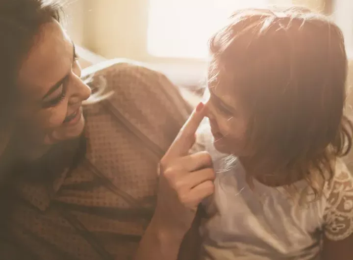 mother touching little girl's face as they smile at each other