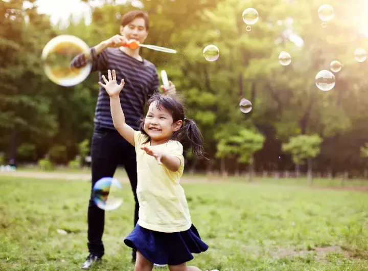 happy little girl blowing bubbles with parent in background